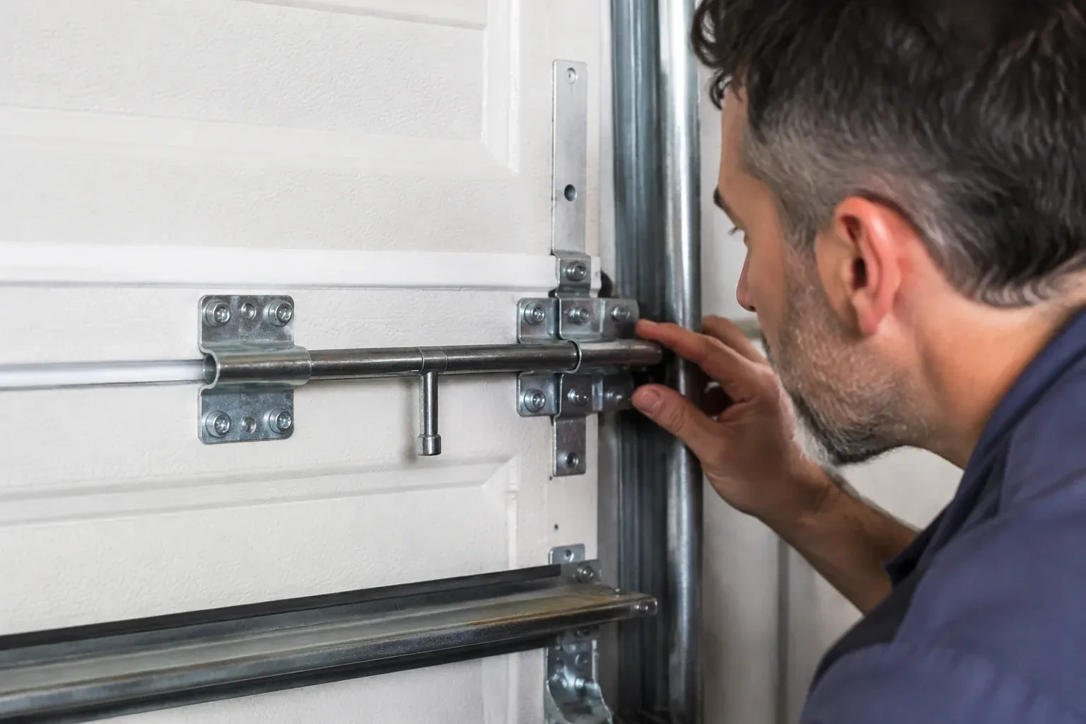 Person leaning close to a white paneled door, one hand on a metal slide-bolt bar mounted across the panel. — Garage Door Manual Lock Repair, Whitby