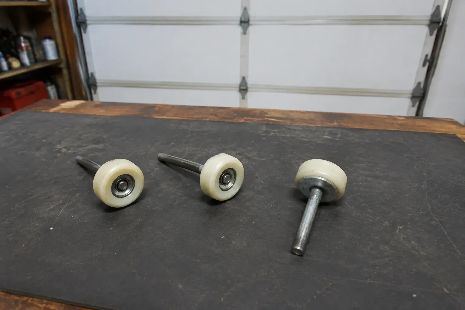 Three detached nylon-wheel garage door rollers with steel stems on a work mat. — Garage Door Roller Replacement, Whitby