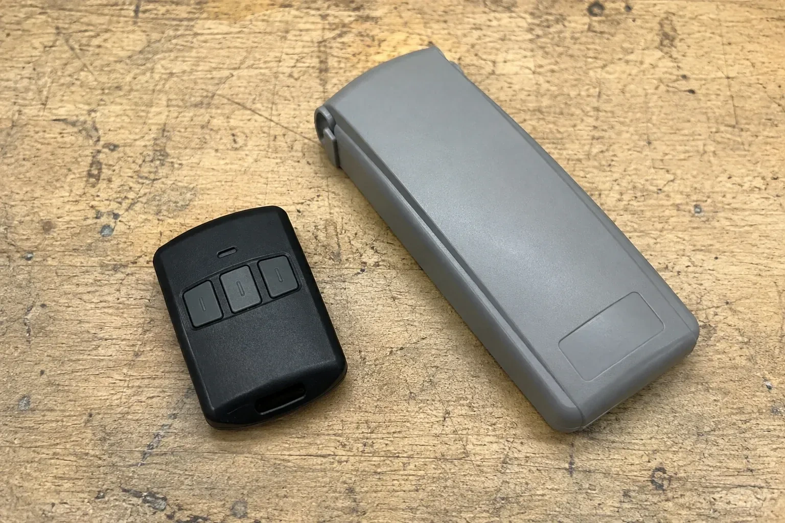 Three-button remote beside a closed grey keypad cover on a workbench. — Garage Door Remote and Keypad Programming, Whitby